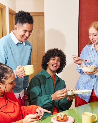 Gruppo di persone sedute a un tavolo mentre condividono cibo e bevande in un clima informale.