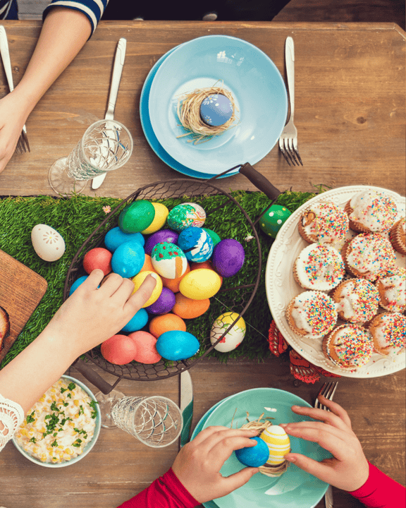 Tavola apparecchiata per Pasqua con mani che raccolgono uova colorate